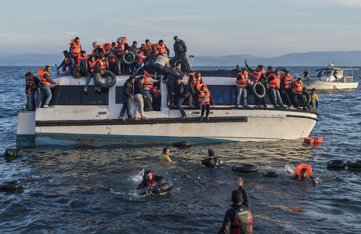 Many refugees on a boat and in the water